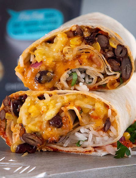 Two veggie burritos cut in half, showing a filling of rice, black beans, corn, vegetables, and melted cheese, stacked on a tray.