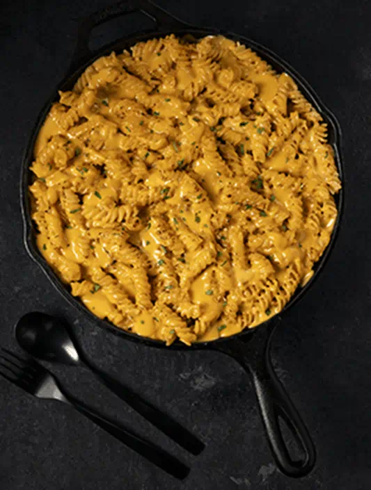 Fusilli pasta in a skillet with cheesy sauce made from Violife dairy-free cheese shreds