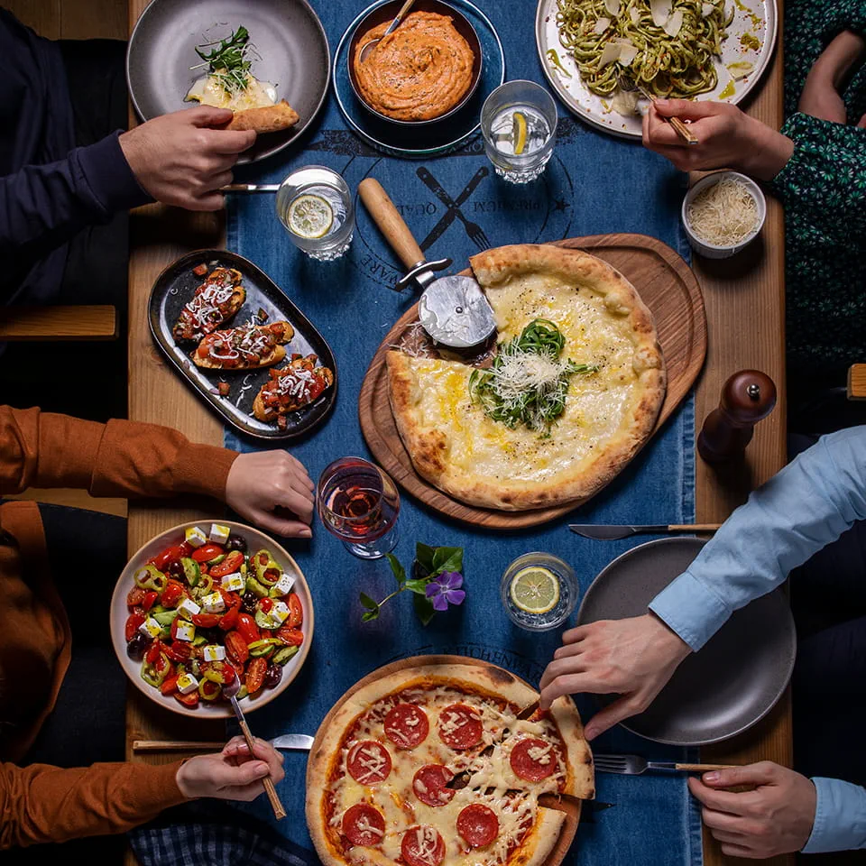 People sitting around a table eating pizza, bruschetta, Greek salad, pasta, and dip made with Violife dairy-free products