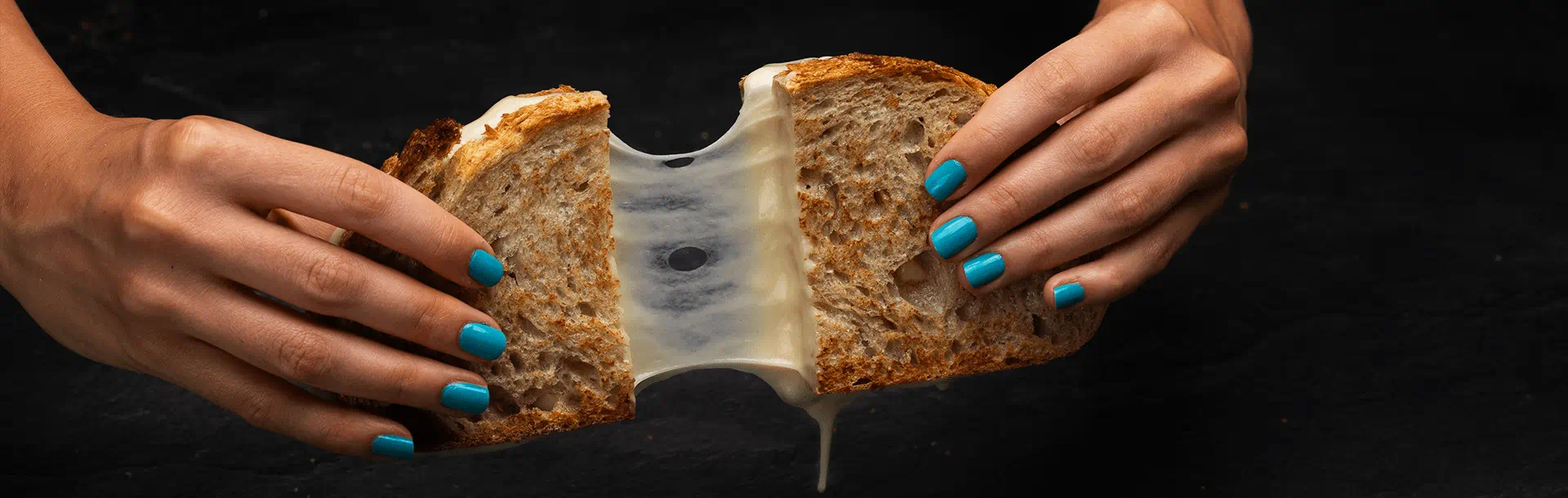 A toasted sandwich is being pulled open by two hands, exposing a smooth, stretchy layer of melted dairy free cheese stretching between the bread slices.