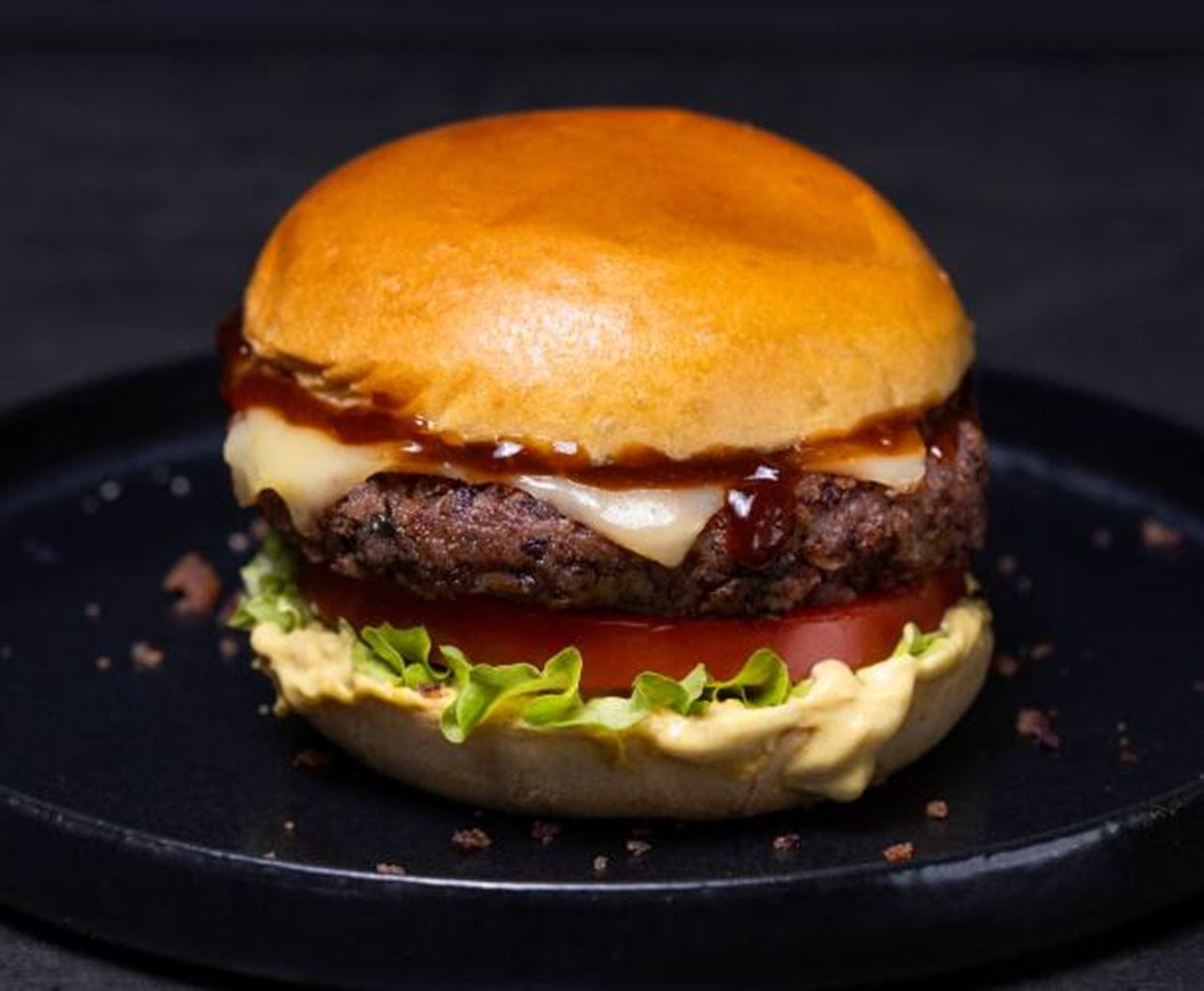 A bean burger made with a bean patty, a Violife dairy free slice, a slice of fresh tomato, green lettuce and a layer of creamy mustard spread.