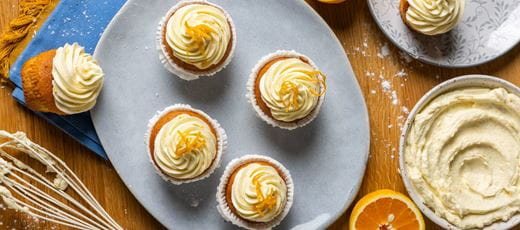 Cupcakes topped with cream cheese frosting. Each cupcake has a swirl of smooth, dairy free cream cheese frosting garnished with thin strips of orange zest.