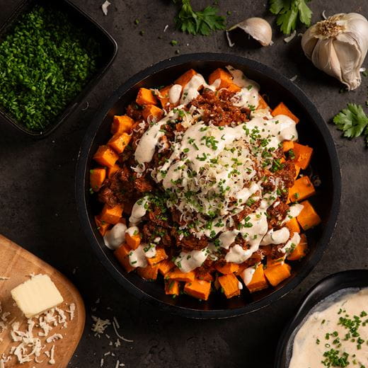 Buddha bowl full of plant-based proteins, fresh veggies and vegan minced meat. Creamy dairy free cream cheese dressing on top and a sprinkle of finely chopped fresh herbs.