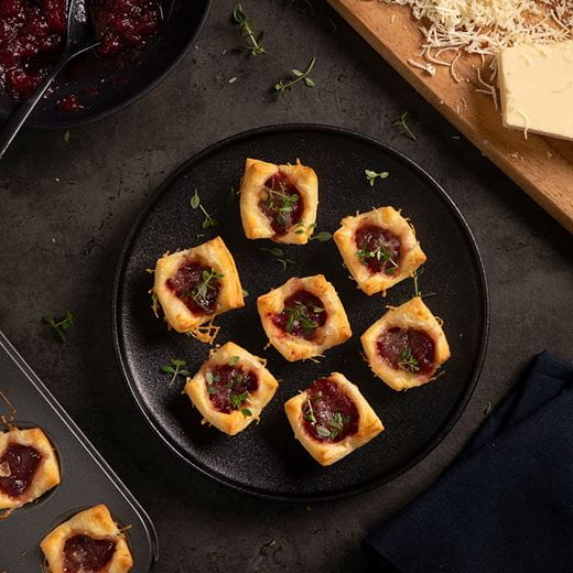 Golden-brown puff pastry bites filled with cranberry sauce, melted dairy free cheese shreds and fresh thyme leaves.