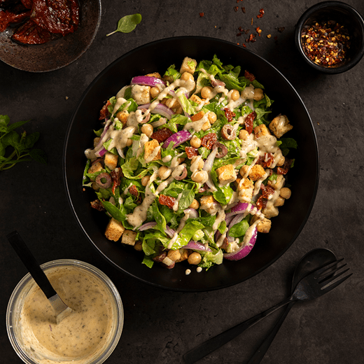 High protein salad with lettuce, chickpeas, red onions, sun-dried tomatoes, croutons and olives drizzled with dairy free cream cheese and tahini dressing.