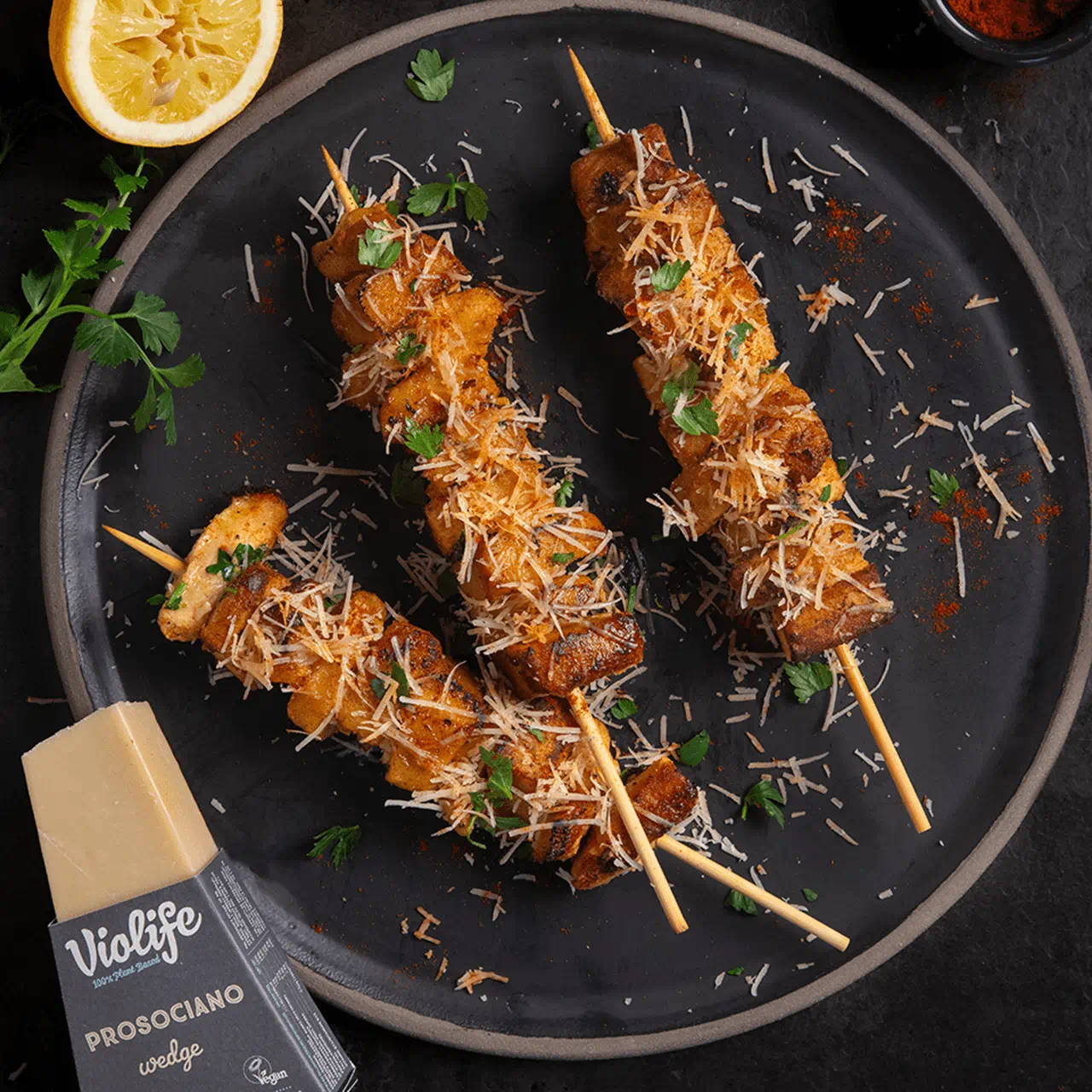 Three wooden skewers threaded with vegan chicken, sprinkled with finely grated Violife Parm and garnished with chopped parsley leaves.