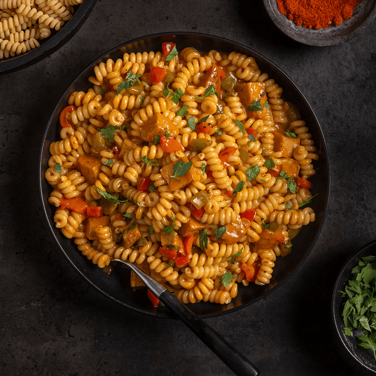 A bowl filled with pasta, pieces of red and green bell peppers and vegan chicken. Freshly chopped parsley sprinkled on top.