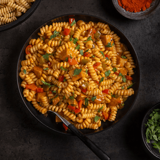 A bowl filled with pasta, pieces of red and green bell peppers and vegan chicken. Freshly chopped parsley sprinkled on top.
