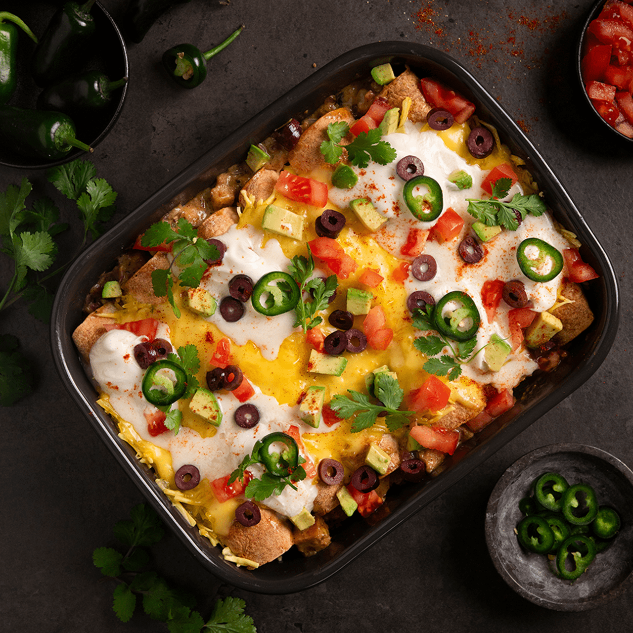 A baking dish with vegan enchiladas verde, topped with melted dairy free cheese, corn, pepper, cilantro and thinly sliced onions.