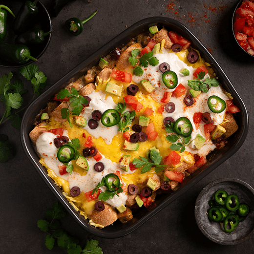 A baking dish with vegan enchiladas verde, topped with melted dairy free cheese, corn, pepper, cilantro and thinly sliced onions.