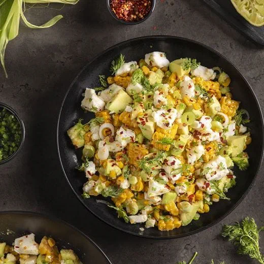 Mexican street corn salad with corn kernels mixed with chunks of avocado, crumbled dairy free cheese, sliced fresh onions and coriander leaves.