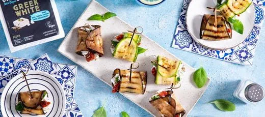 Eggplant and zucchini rolls, each secured with a wooden skewer. Rolls are filled with dairy free cheese in crumbles, basil and sun-dried tomatoes.