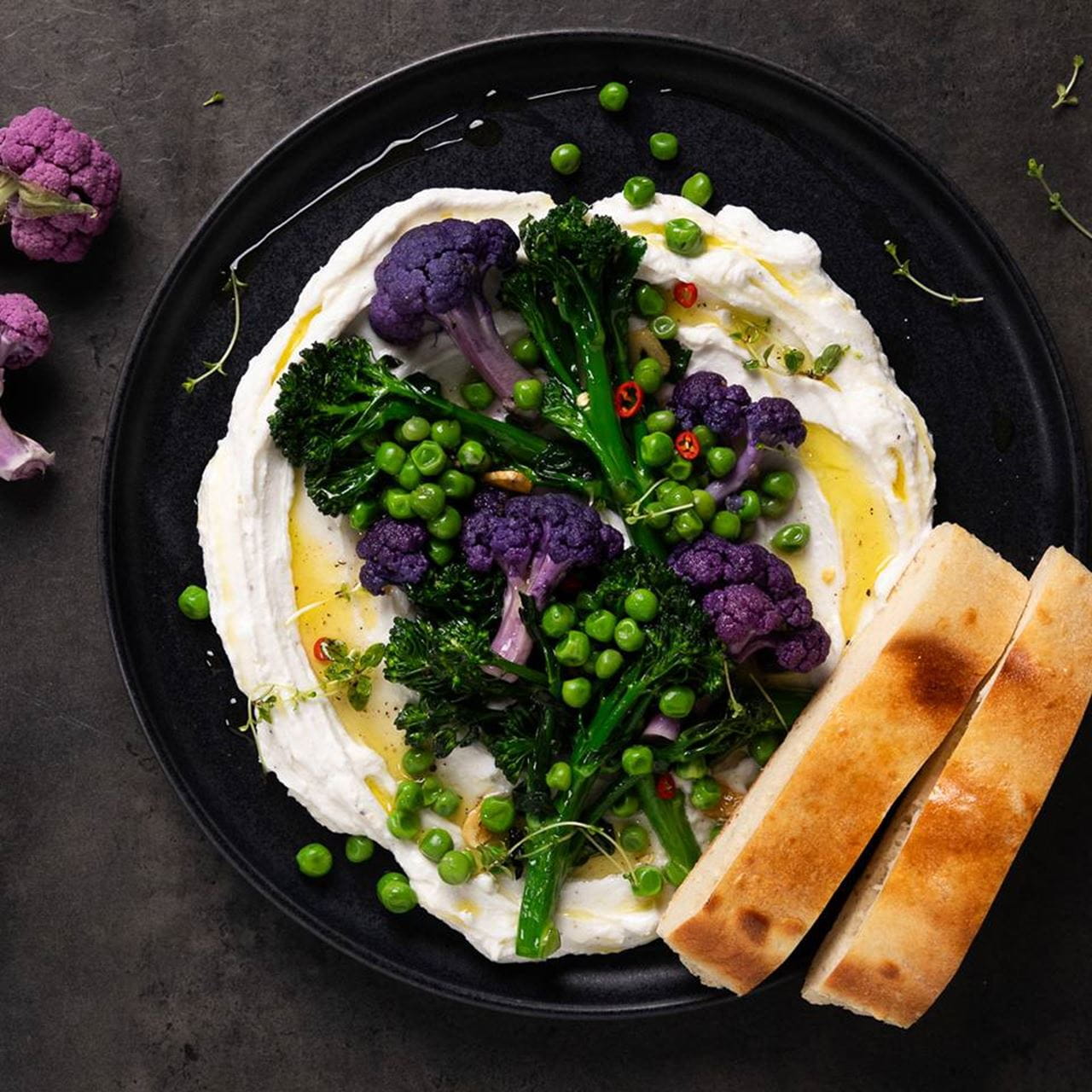 Purple Broccoli Salad in a black plate featuring purple broccoli, broccolini, green peas and creamy dairy free cheese spread drizzled with olive oil.