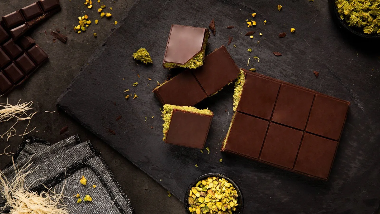 Dubai Chocolate Bars with a green pistachio filling made with dairy free cream cheese, cut into squares and placed on a black slate board.