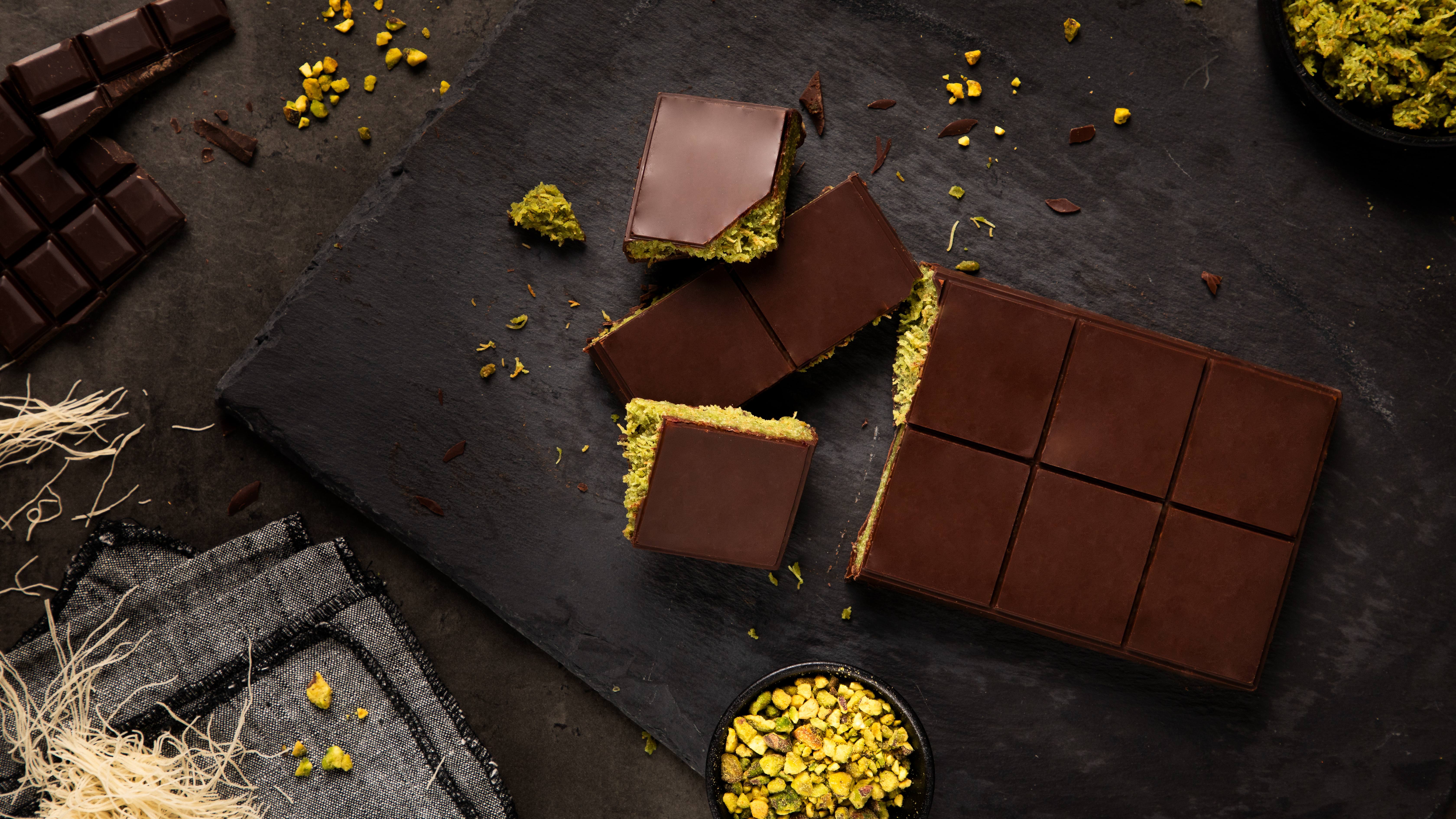 Dubai Chocolate Bars with a green pistachio filling made with dairy free cream cheese, cut into squares and placed on a black slate board.