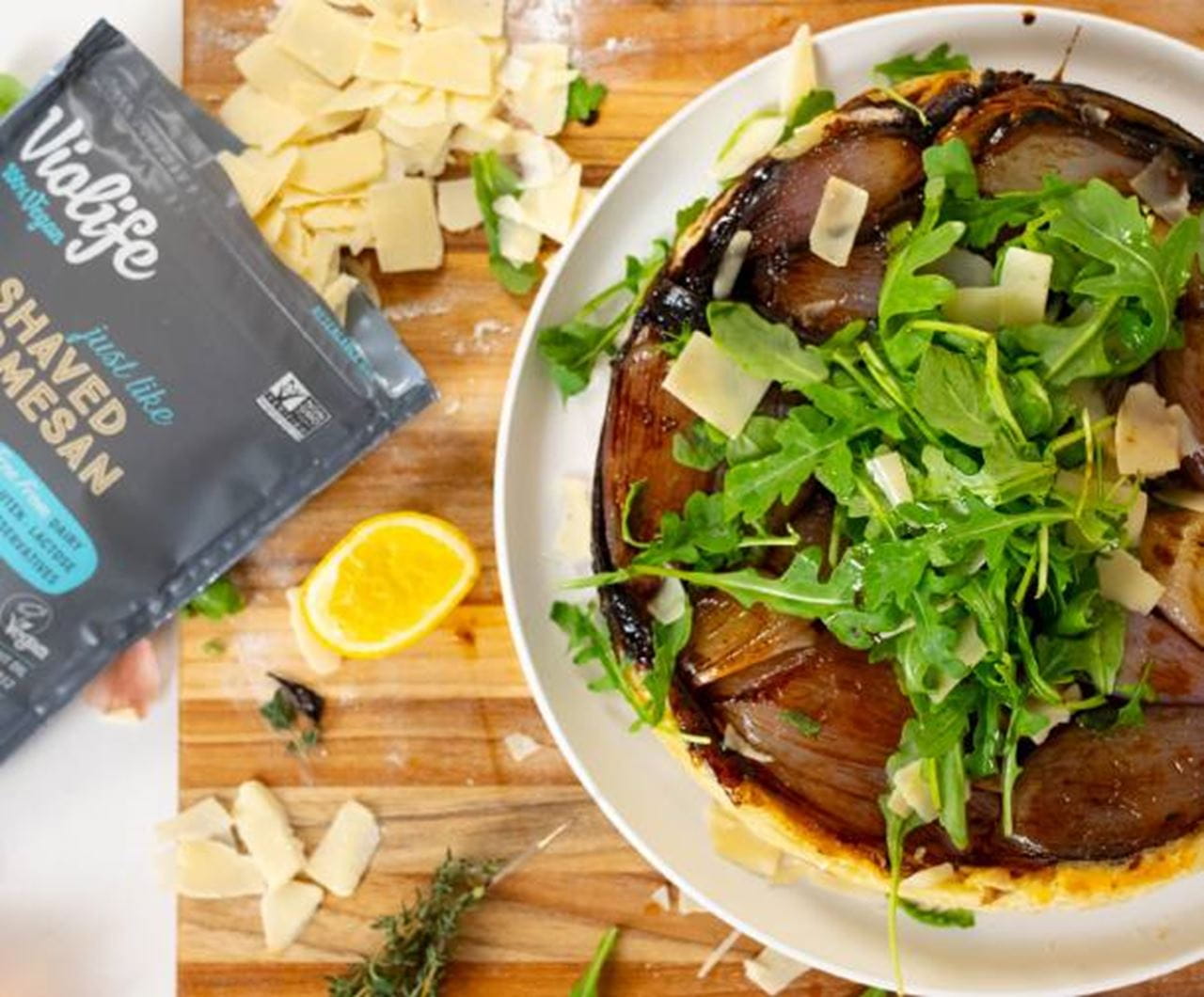 A caramelized shallot tarte tatin, topped with fresh arugula and Shaved dairy free Parmesan. On the left, a bag of Violife cheese alternative.
