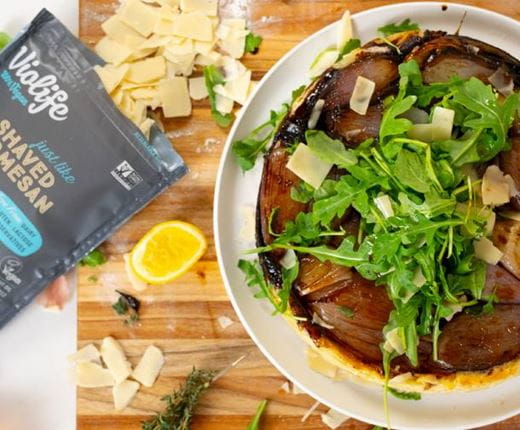 A caramelized shallot tarte tatin, topped with fresh arugula and Shaved dairy free Parmesan. On the left, a bag of Violife cheese alternative.