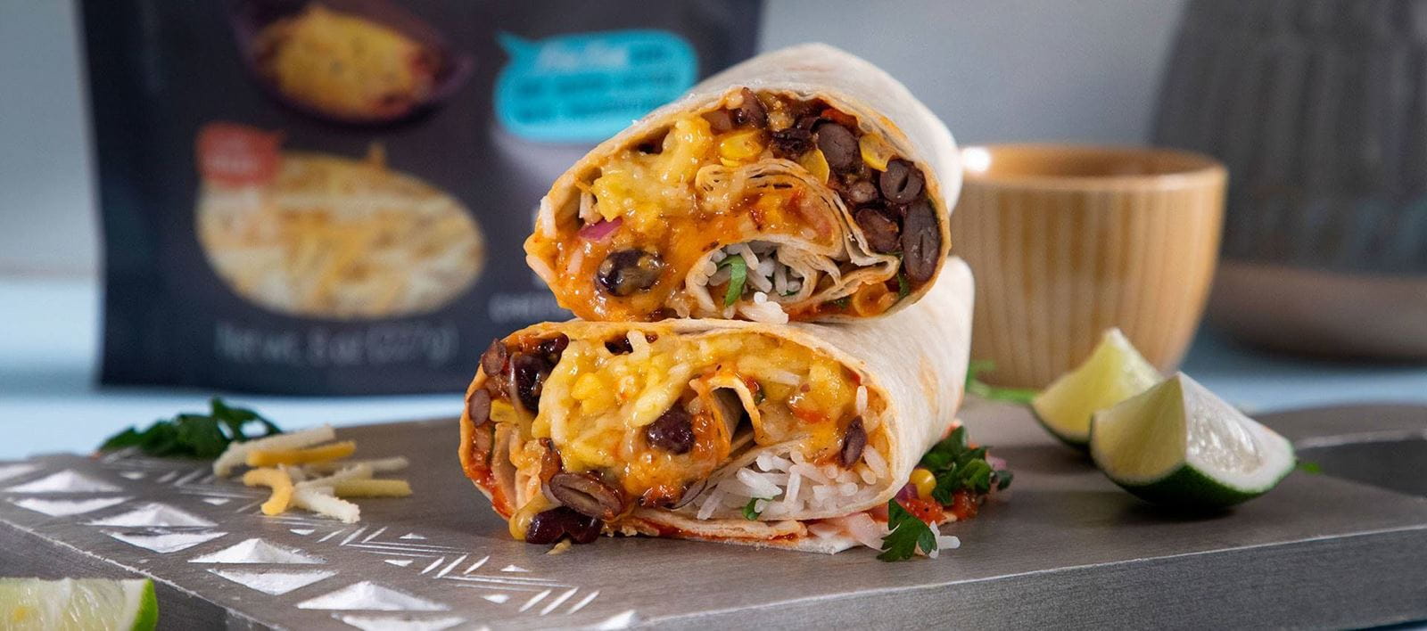 Two halves of a burrito stacked on a wooden board, filled with rice, black beans, corn, melted Violife dairy free cheese shreds and fresh herbs.