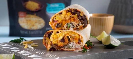 Two halves of a burrito stacked on a wooden board, filled with rice, black beans, corn, melted Violife dairy free cheese shreds and fresh herbs.
