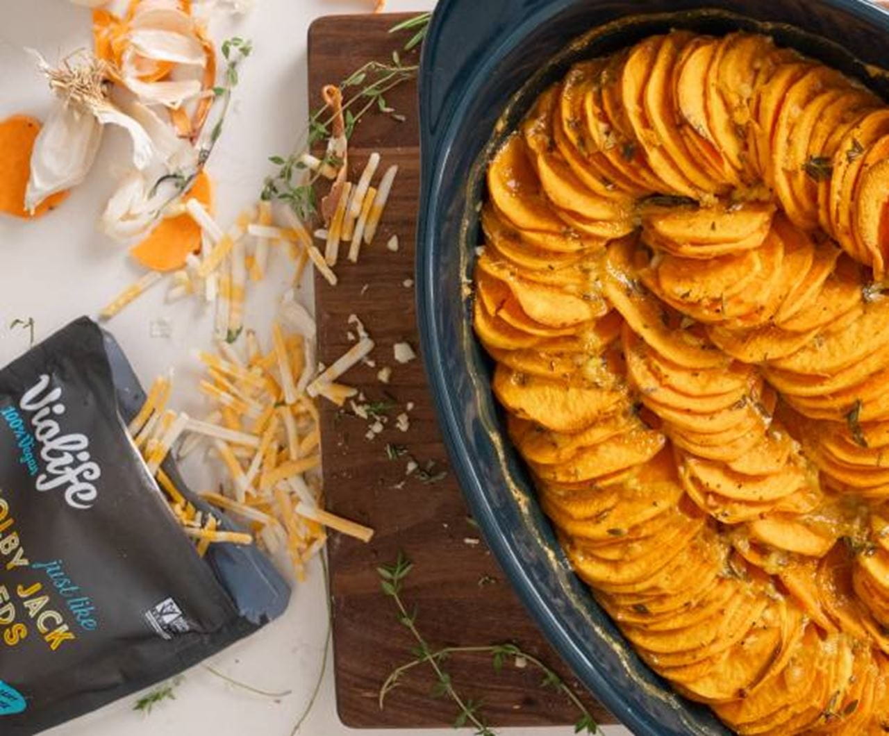 A baking dish filled with neatly layered slices of sweet potato au gratin, baked until tender and golden with herbs and melted dairy free cheese.