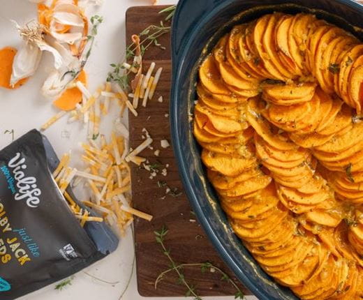 A baking dish filled with neatly layered slices of sweet potato au gratin, baked until tender and golden with herbs and melted dairy free cheese.