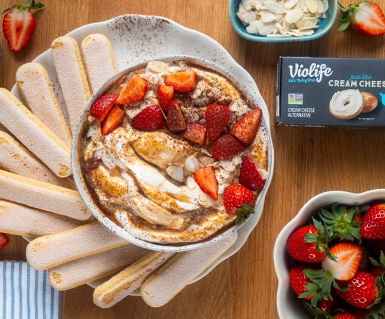 Creamy Martini Dip swirled with dairy free cream cheese, topped with sliced strawberries, flaked almonds and some cocoa powder, surrounded by ladyfingers.