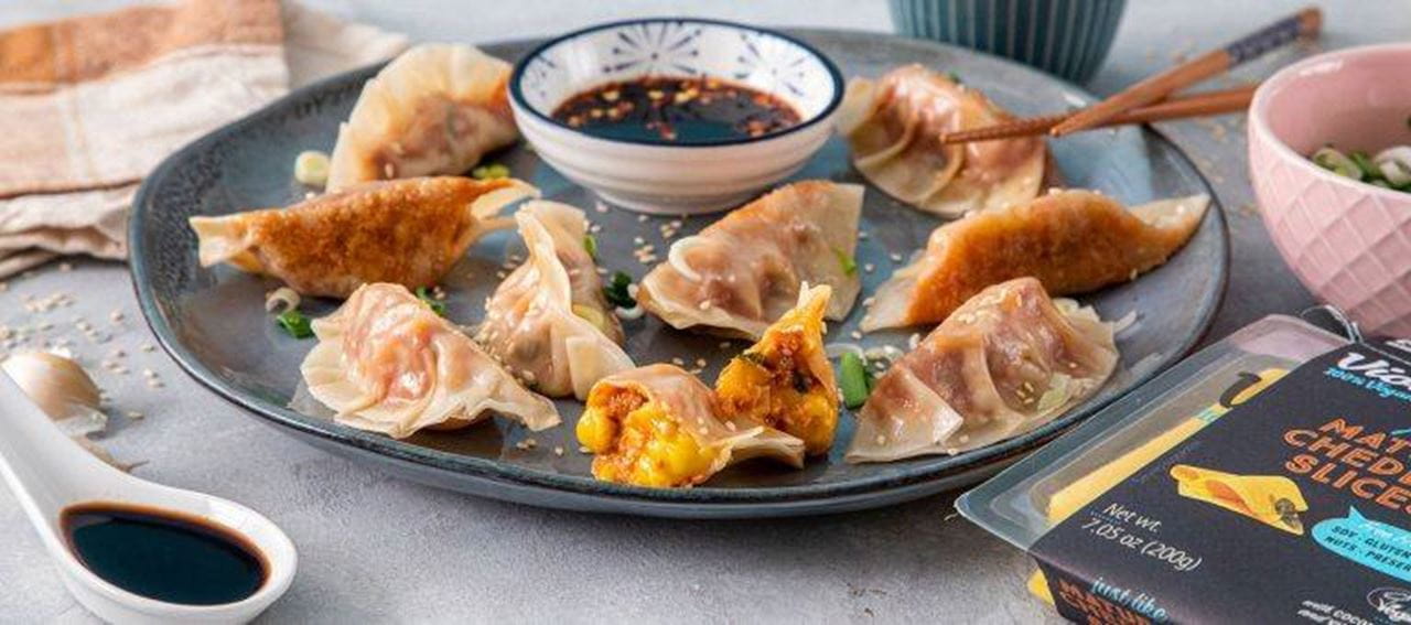 Cheeseburger dumplings, one dumpling is open to show melted dairy free cheese and vegan minced meat filling. A small bowl of dipping sauce is in the center.