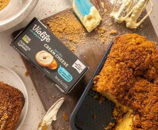 Crumb‑topped dairy free cream cheese coffee cake in a baking pan, with a slice removed to show its soft interior.