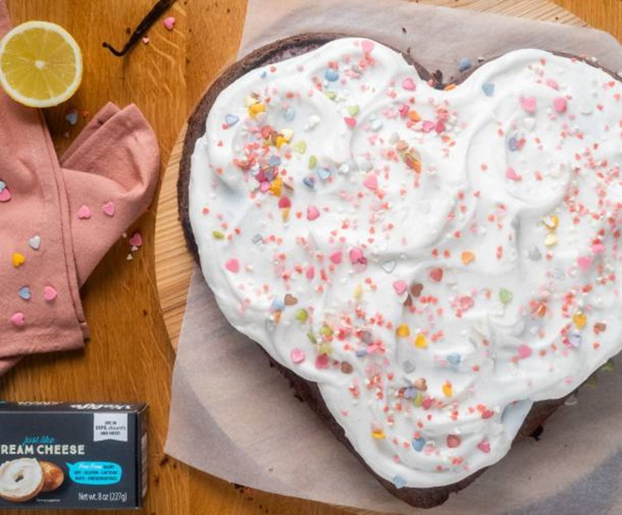 Heart‑shaped Valentines Day Cake topped with swirls of dairy free cream cheese frosting and colorful heart‑shaped sprinkles.