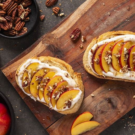 Two slices of toasted bread topped with a layer of dairy free cream cheese spread, thinly sliced fresh peaches and chopped pecans.