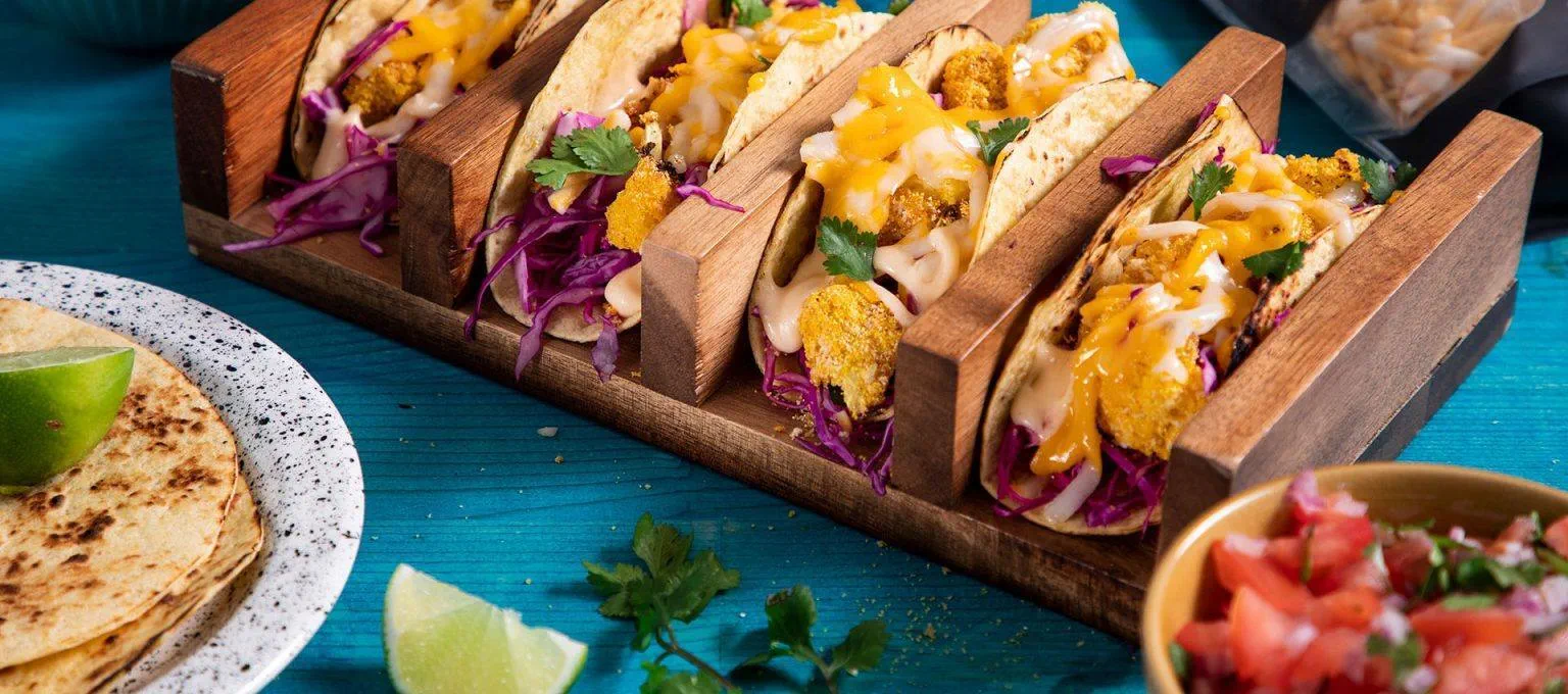Four cauliflower tacos arranged in a wooden taco holder, filled with crispy roasted cauliflower, purple cabbage, dairy free sauce and fresh cilantro.