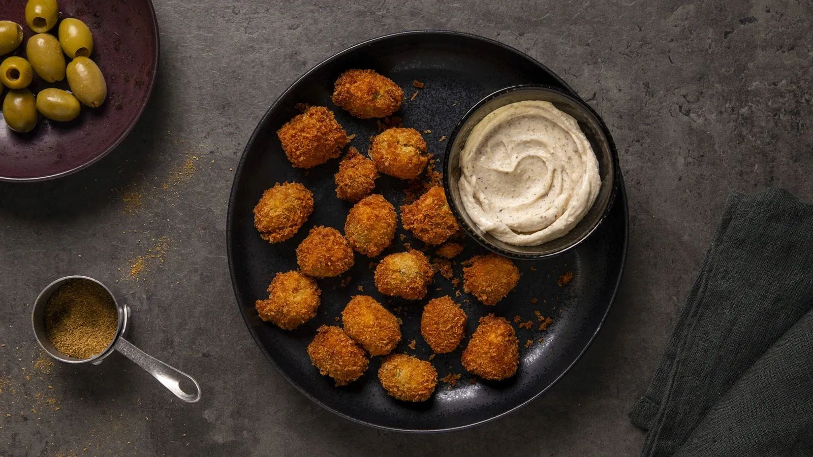 Golden, crispy fried olives arranged around a bowl with a creamy dairy free cream cheese dipping sauce.