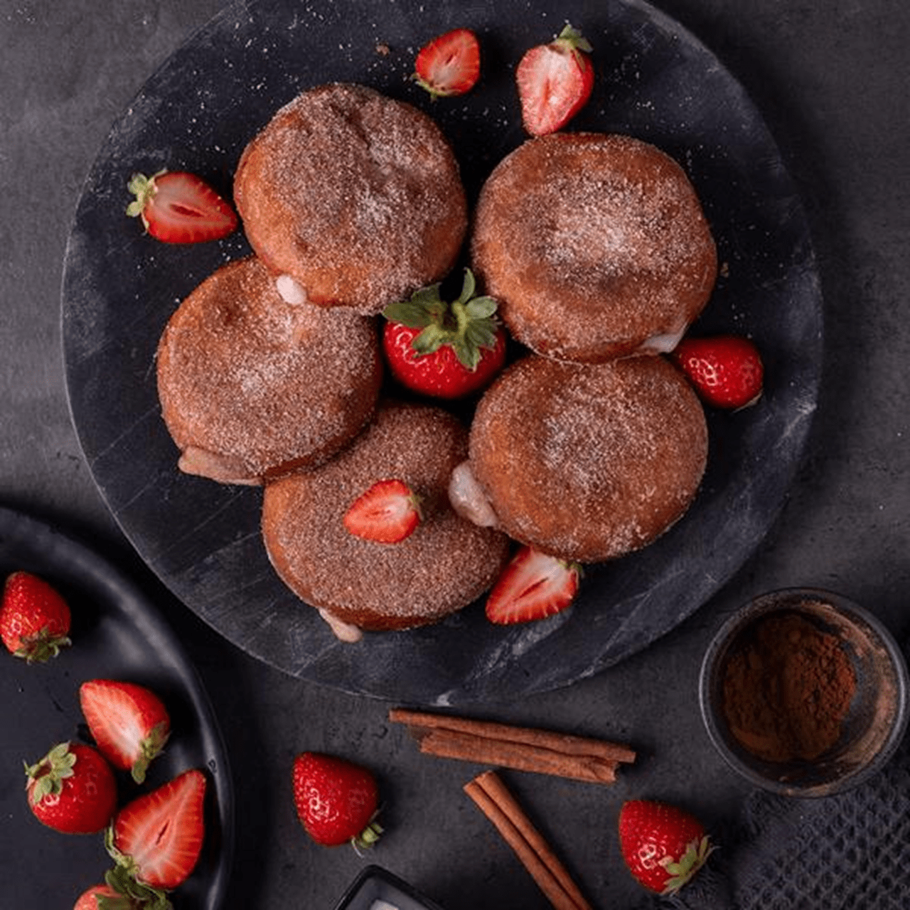Donut holes - small, round pastries filled with supreme cream cheese that are golden brown and evenly coated with a layer of granulated or powdered sugar.