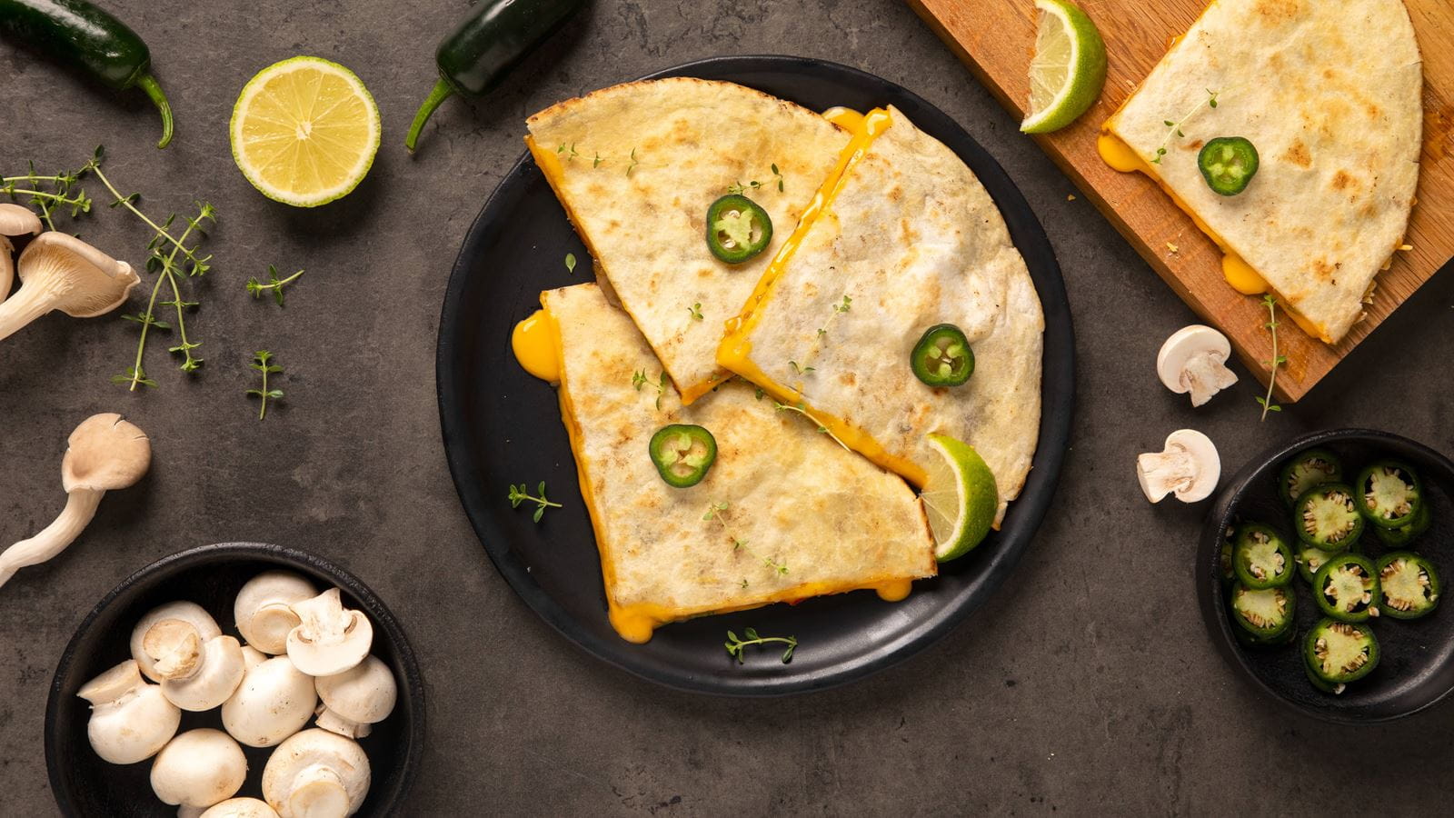 A sliced quesadilla filled with dairy free melted cheese, mushrooms peppers, garlic, onion and taco seasoning on a black plate