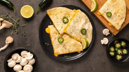A sliced quesadilla filled with dairy free melted cheese, mushrooms peppers, garlic, onion and taco seasoning on a black plate