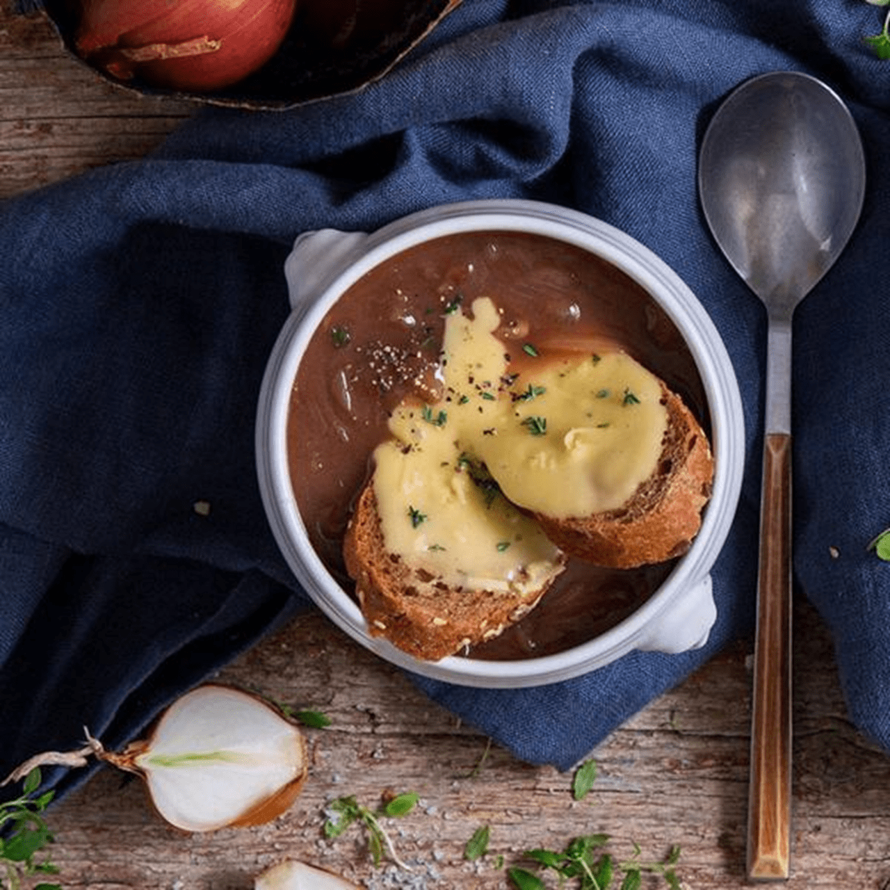 French onion soup topped with toasted bread and melted dairy free cheese and herbs, set on a rustic wooden table.