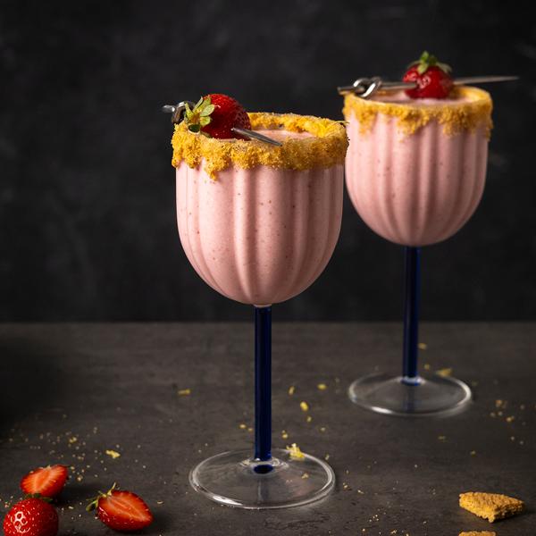Two strawberry martinis in stemmed glasses with crumb‑coated rims, garnished with whole strawberries on cocktail picks, with fresh strawberry slices.