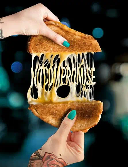 Sandwich grillé garni de tranches de fromage Violife fondante et 100% vegan, accompagné de la mention « Sans compromis »