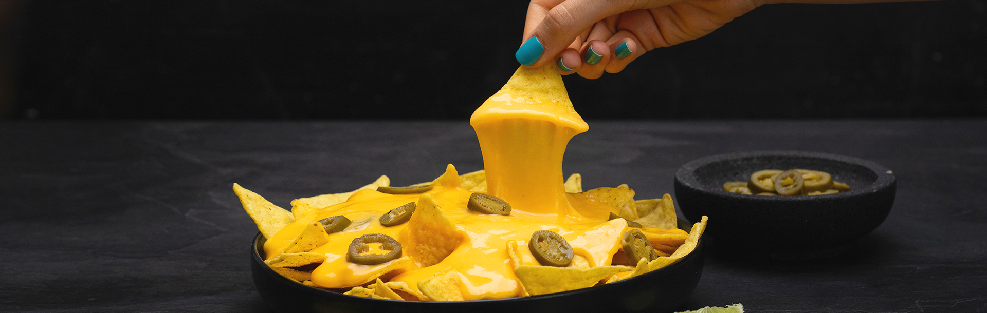 Main trempant une tortilla dans une sauce chaude de Violife, l'alternative végétale au fromage, sans produits laitiers, avec nachos et rondelles de jalapeño en dessous