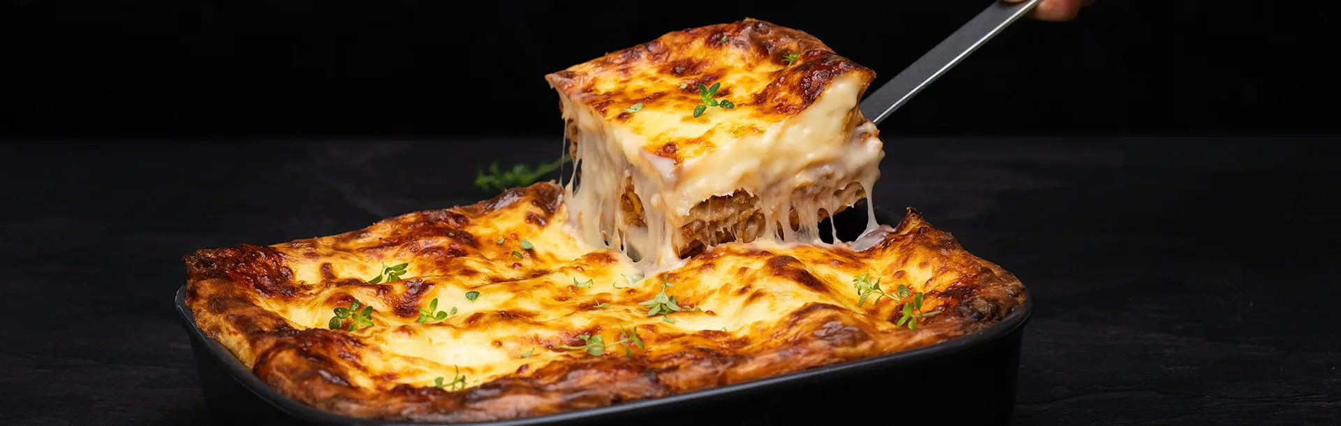 Gros plan sur une part de lasagnes soulevée, laissant apparaître Violife l'alternative végétale au fromage, sans produits laitiers, fondu et doré, qui s’étire dans un plat tout juste sorti du four.