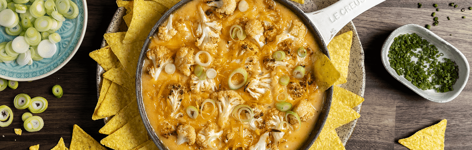 Poêle remplie de sauce faite avec Violife l'alternative végétale au fromage, de fleurettes de chou‑fleur rôties et d’oignons nouveaux, servie avec une assiette de tortillas